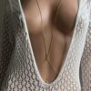Bijou de corps doré minimaliste pour femme porté sur une robe en crochet blanc avec un décolleté profond, parfait pour sublimer une tenue estivale boheme chic