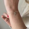 N6162 Bracelet croix femme Argent 925 massif minimaliste - Bijoux Bracelets femmes en ligne Ninanina Bijou artisanal minimaliste porté sur une main en l'air : bracelet croix en argent massif 925 pour femme, signé Ninanina