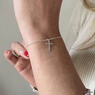 Bijou artisanal minimaliste porté sur une main en l'air : bracelet croix en argent massif 925 pour femme, signé Ninanina