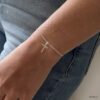 N6162a Bracelet croix femme Argent 925 massif minimaliste - Bijoux Bracelets femmes en ligne Ninanina Bracelet croix en argent 925 massif pour femme porté sur une main qui pend le long d'un pantalon, au design minimaliste, fait main par Ninanina
