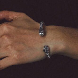 Zoom sur le bracelet homme avec design tête de mort en acier tressé et boules aux extrémités porté sur une main d'homme - Accessoire chic et audacieux