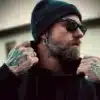 N7361 Boucle d'oreille homme creole fine Acier Inoxydable - Bijoux Boucles d oreilles en ligne Ninanina Boucle d’oreille homme en acier inoxydable, créole minimaliste de 20 mm pour un style épuré portée par un homme barbu et tatoué avec lunettes et bonnet noir