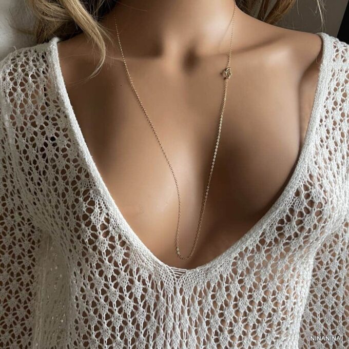 Sautoir féminin en or laminé gold filled 14k avec pendentif infini, fait main Ninanina, accessoire élégant porté avec une tenue blanche crochetée à décolleté plongeant, idéal pour un style bohème chic.