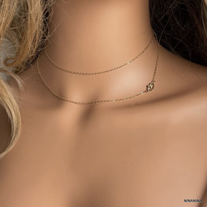 Gros plan sur bijou élégant pour femme, collier sautoir en or laminé gold filled 14k avec symbole infini porté en collier court avec 2 tours autour du cou