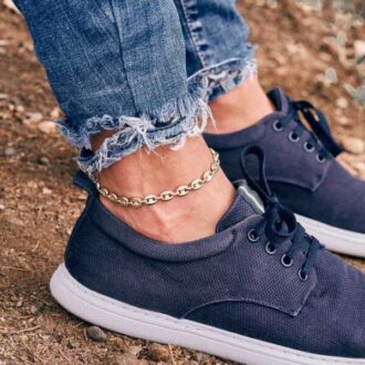 Chaîne de cheville homme en acier inoxydable grain de café portée sur une cheville d'homme portant un jean et des baskets bleues - Bijou artisanal tendance et fait main