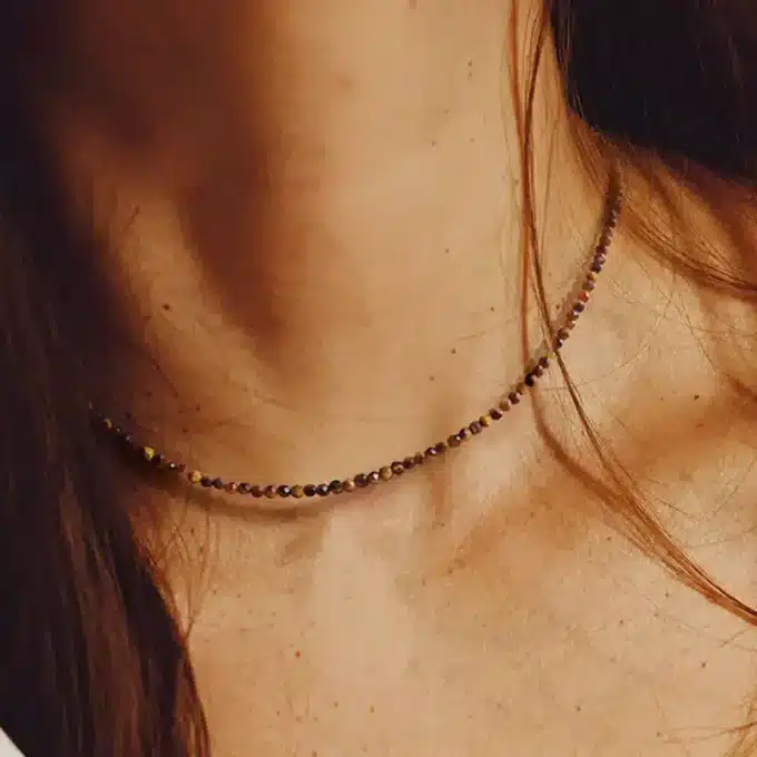 Zoom sur le Collier pour femme en pierres Œil de Tigre à facettes de 2mm portée par une femme aux cheveux longs - Bijou artisanal fait main en France