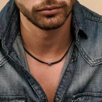 Zoom sur le Collier Cordon Noir Artisanal Perle Cylindrique Acier Inox Made In France porté par un homme barbu avec une chemise en jean