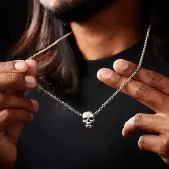 Zoom sur le Collier Pendentif Tete De Mort Homme Acier Inoxydable Made In France par Ninanina porté par un homme qui tient la chaine entre ses doigts