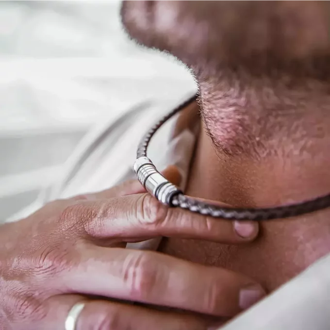 Collier Ras De Cou Homme Cuir Tressé Et Acier Inoxydable Fait Main En France signé Ninanina porté par un homme qui soulève le bijou avec ses doigts