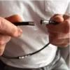Zoom sur le fermoir sécurisé et présenté ouvert du collier Ras De Cou Homme Cuir Tressé Et Acier Inoxydable tenu dans les mains d'un homme